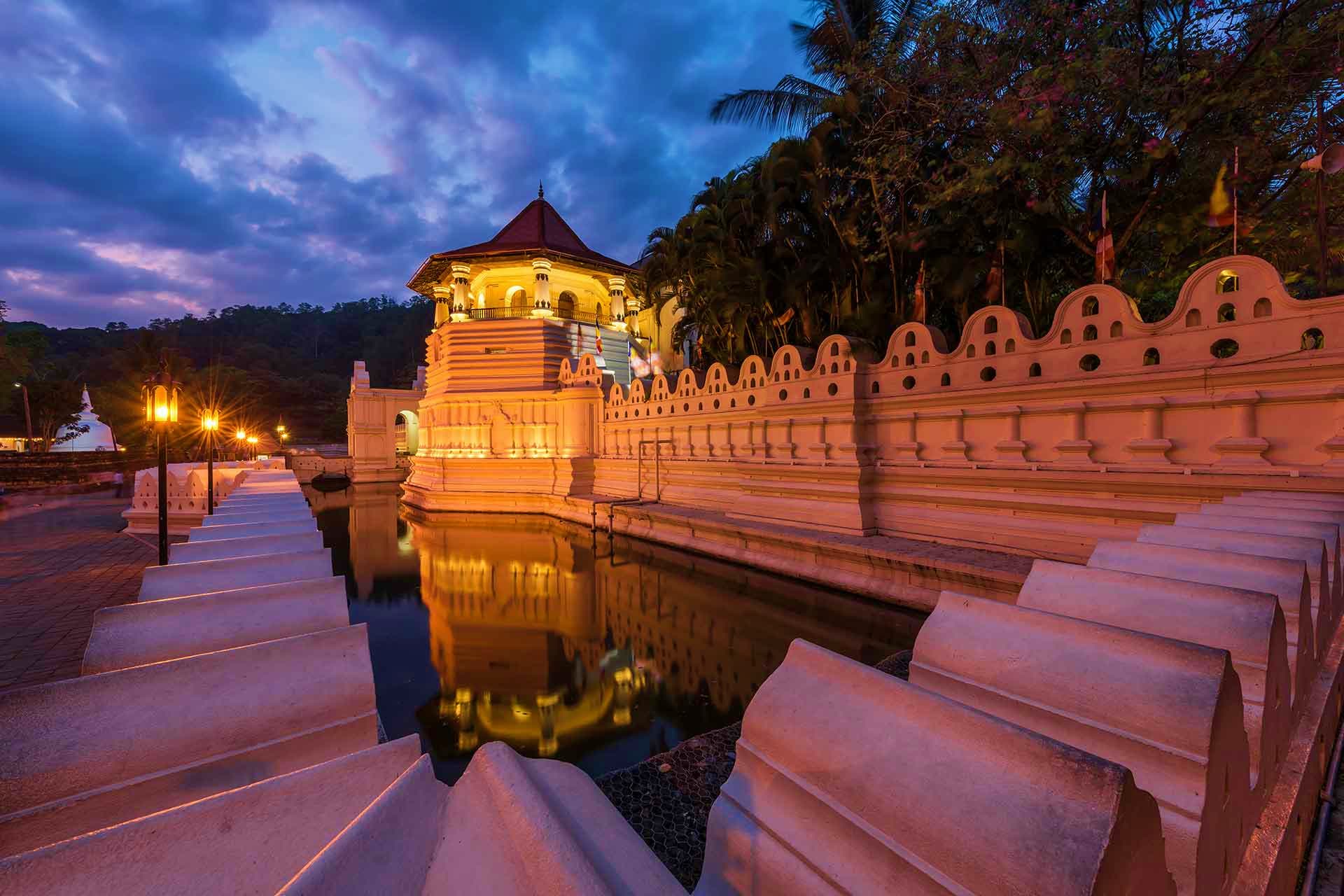 Sri Lanka Visa Sri Lankan Buddhist temple with golden spire and ornate walls reflected in water at twilight, surrounded by palm trees